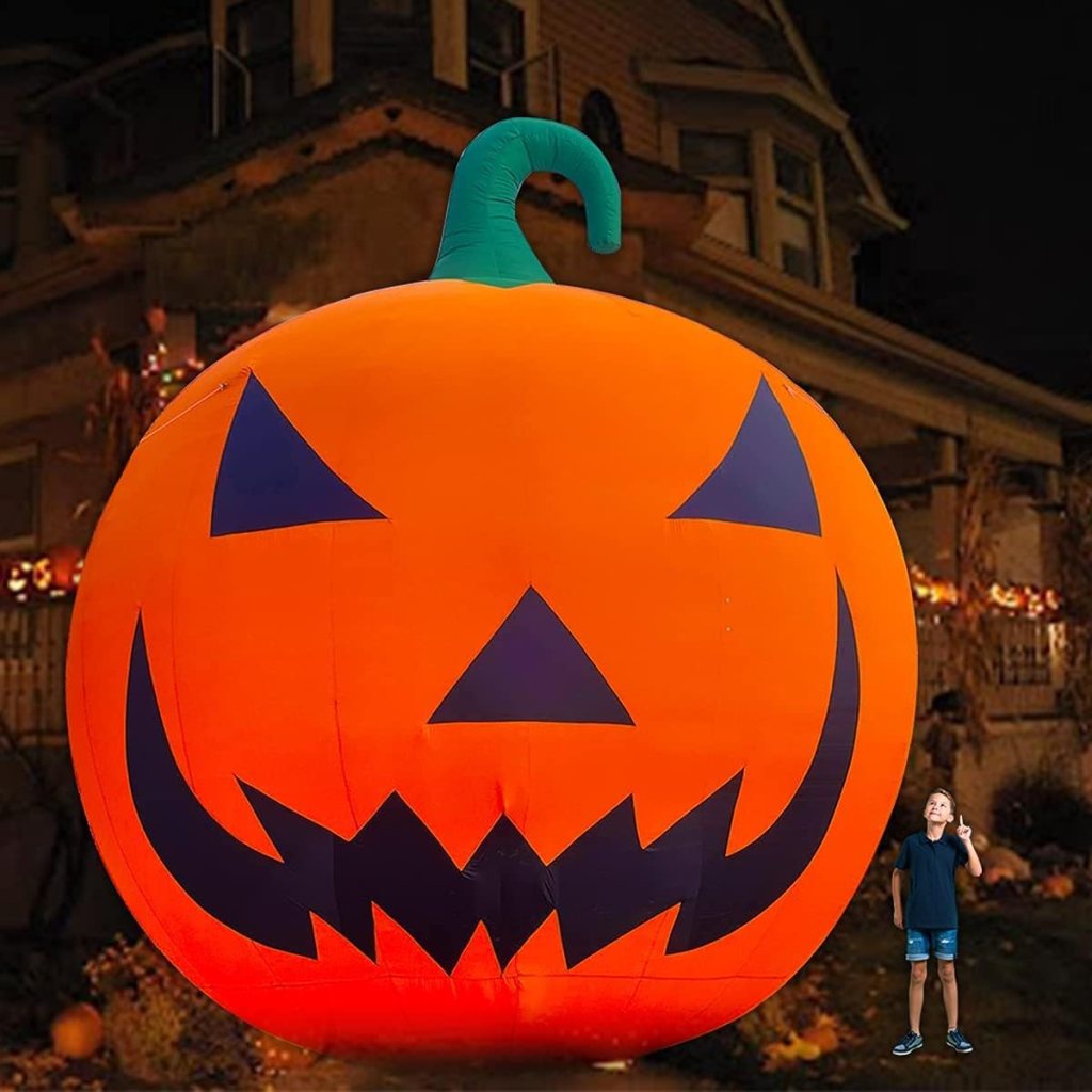 A large inflatable Halloween pumpkin with a menacing face, set against a backdrop of a house decorated for the holiday. A child stands next to the pumpkin, making a peace sign.