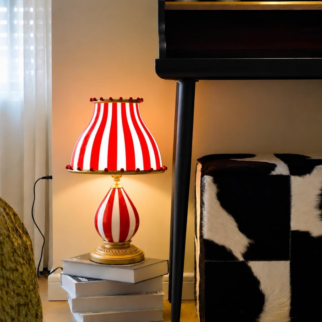 A decorative lamp with a red and white striped shade stands on a stack of books beside a black and white patterned stool.