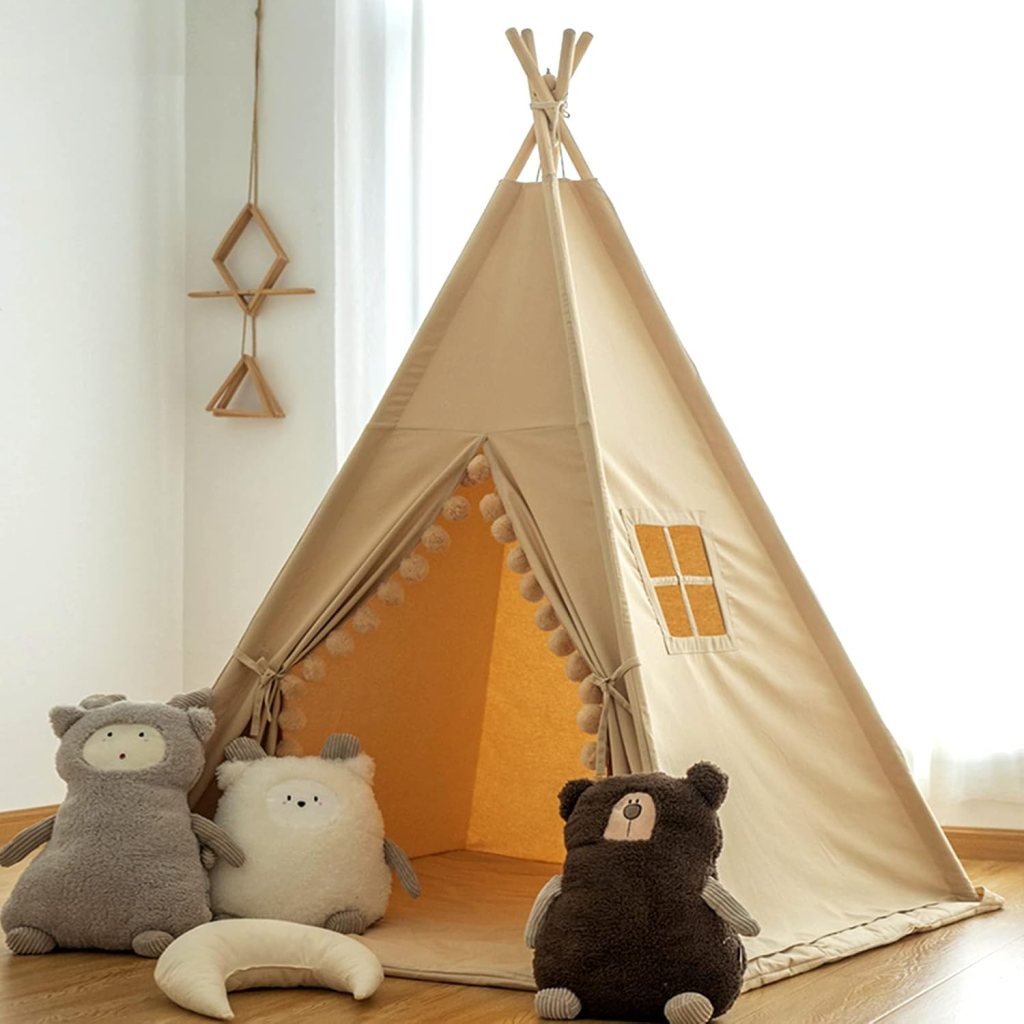 A fabric teepee play tent with a warm yellow interior, decorated with pom-poms along the entrance. Three plush stuffed animals sit outside the tent: a gray bear, a white round bear, and a dark brown bear. Wooden decor is visible on the wall.
