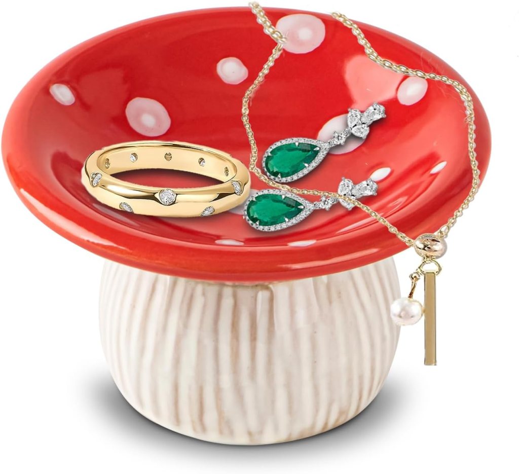 A decorative red dish with white polka dots, holding a gold ring, emerald earrings, and a pearl necklace.