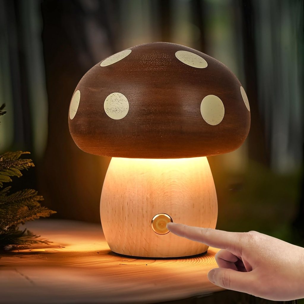 A wooden mushroom-shaped lamp with a brown cap and white polka dots, emitting warm light, with a hand pressing the switch on its base.