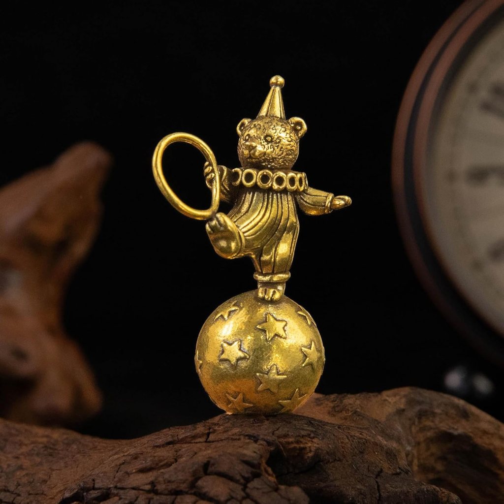 A golden figurine of a bear wearing a party hat, balancing on a star-embellished ball while holding a hoop.