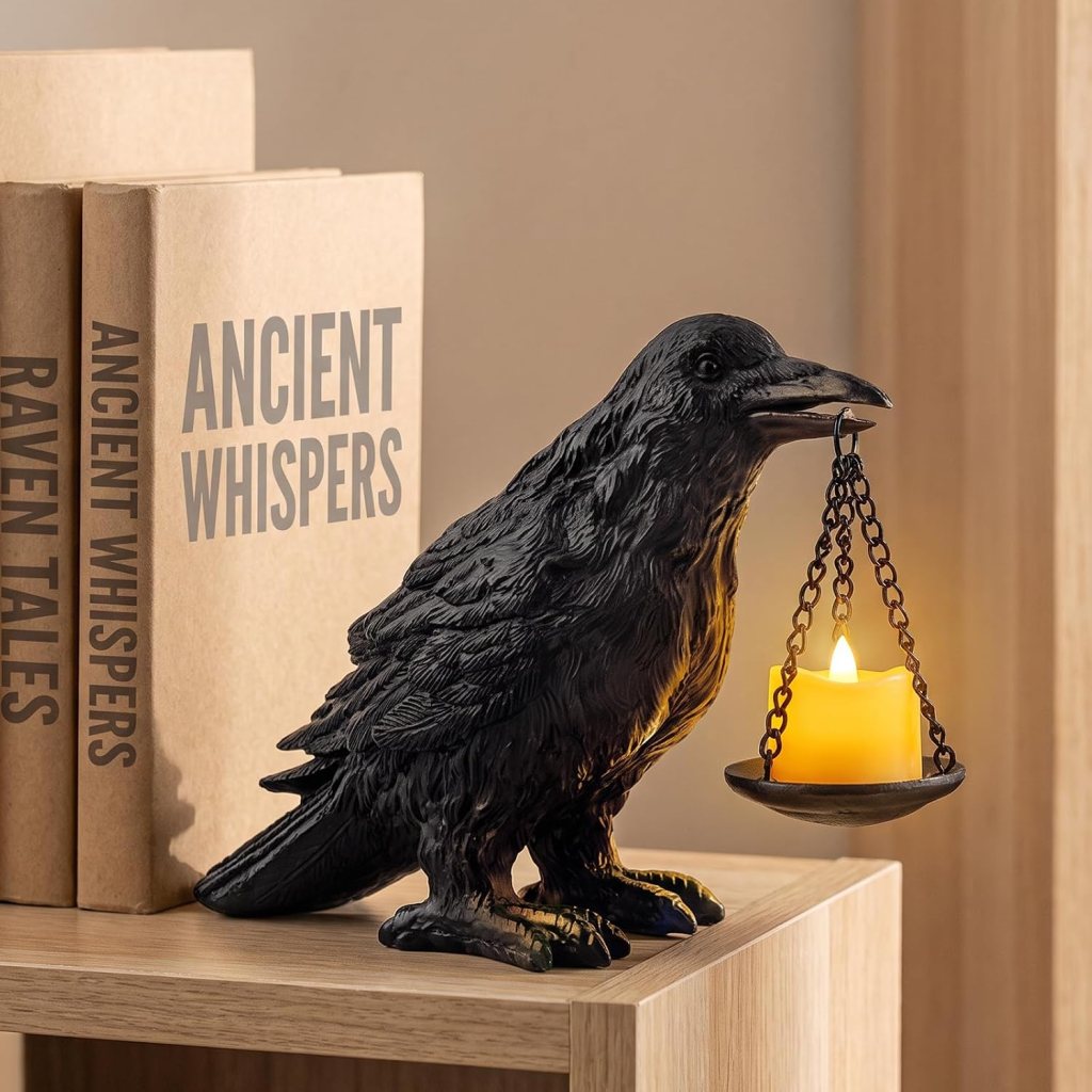 A black raven figurine holding a small candle holder with a lit candle, displayed on a wooden shelf next to books titled 'ANCIENT WHISPERS' and 'RAVEN TALES'.