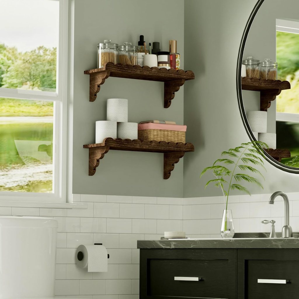 A modern bathroom featuring two wooden floating shelves with various toiletries, including glass jars, lotion bottles, and a woven basket. White rolled towels are placed on the lower shelf, next to a toilet and a sink with a dark cabinet. A round mirror reflects a view of greenery outside through a window.