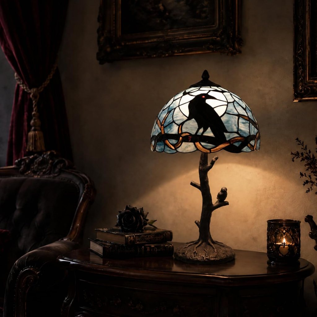 A stained glass lamp with a raven design, illuminating a vintage wooden table accompanied by books and a candle in a dimly lit room.