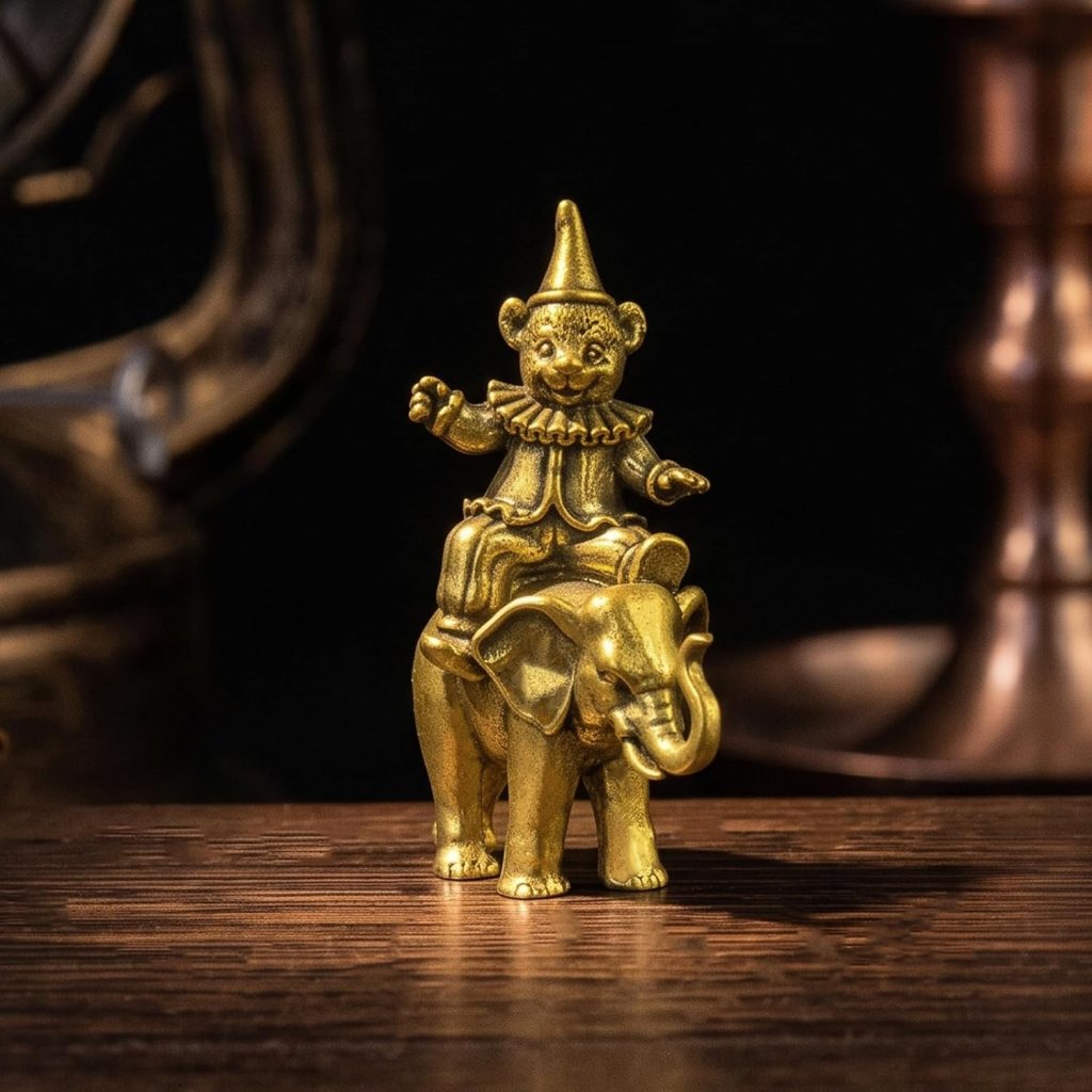A golden figurine depicting a seated clown on an elephant, showcasing intricate details and a shiny finish.