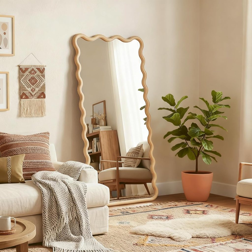 A stylish living room featuring a wavy-edged mirror, a cozy sofa with decorative pillows, a woven throw blanket, a potted fiddle leaf fig plant, and a light-colored rug with intricate patterns.