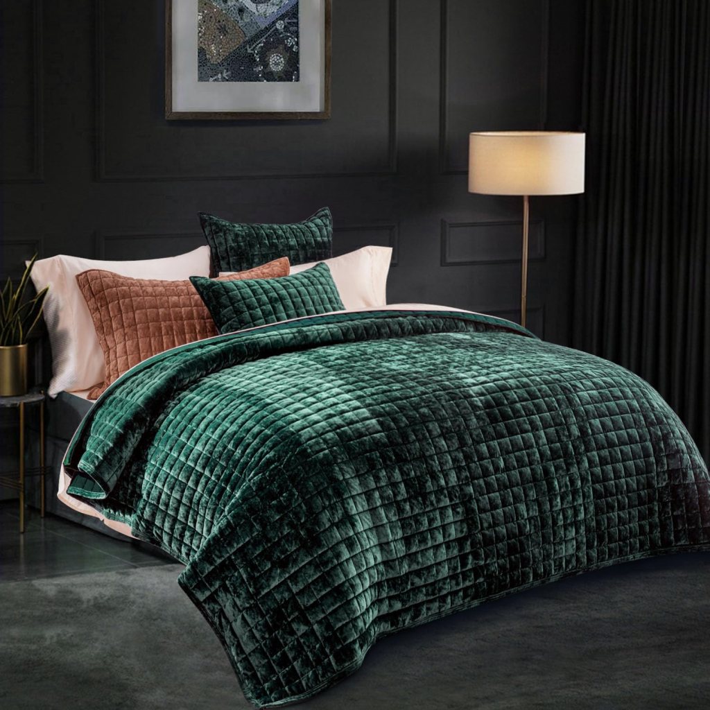 A stylish bedroom featuring a deep green quilted bedspread, accented with matching green and a brown decorative pillows, alongside a modern lamp and dark wall decor.