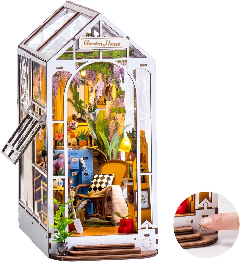 A detailed miniature model of a garden house, featuring a transparent structure with plants, a cozy chair, and decorative elements inside. The exterior has a sign reading 'Garden House' and a small section highlighting an interactive feature.