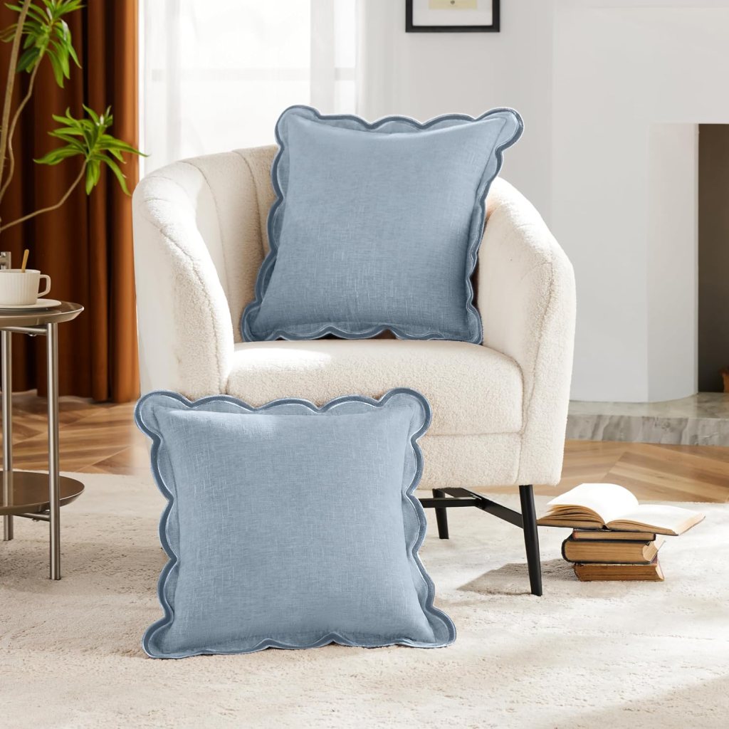 Light blue decorative pillows with scalloped edges placed on a cream-colored sofa in a cozy living room setting.