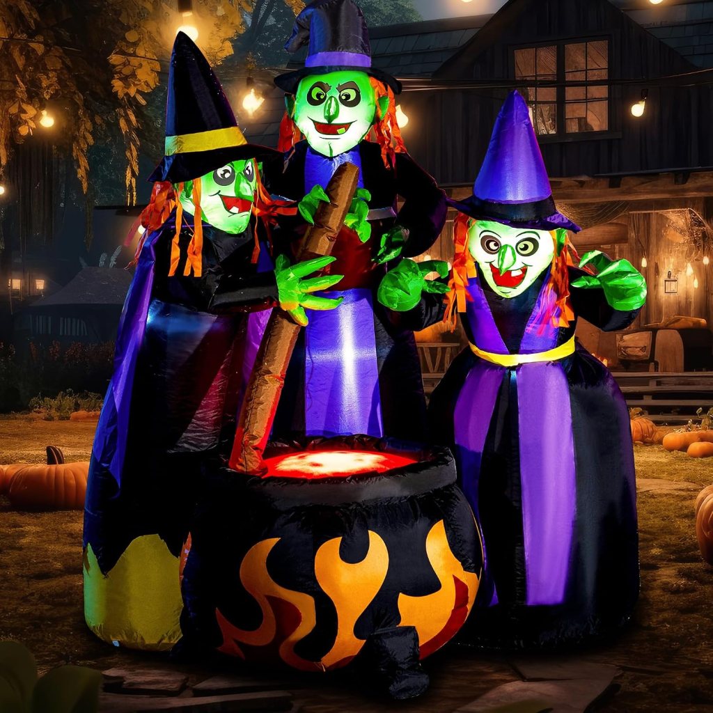 Three inflatable witches with green faces and colorful outfits gather around a bubbling cauldron, set against a festive outdoor Halloween backdrop.