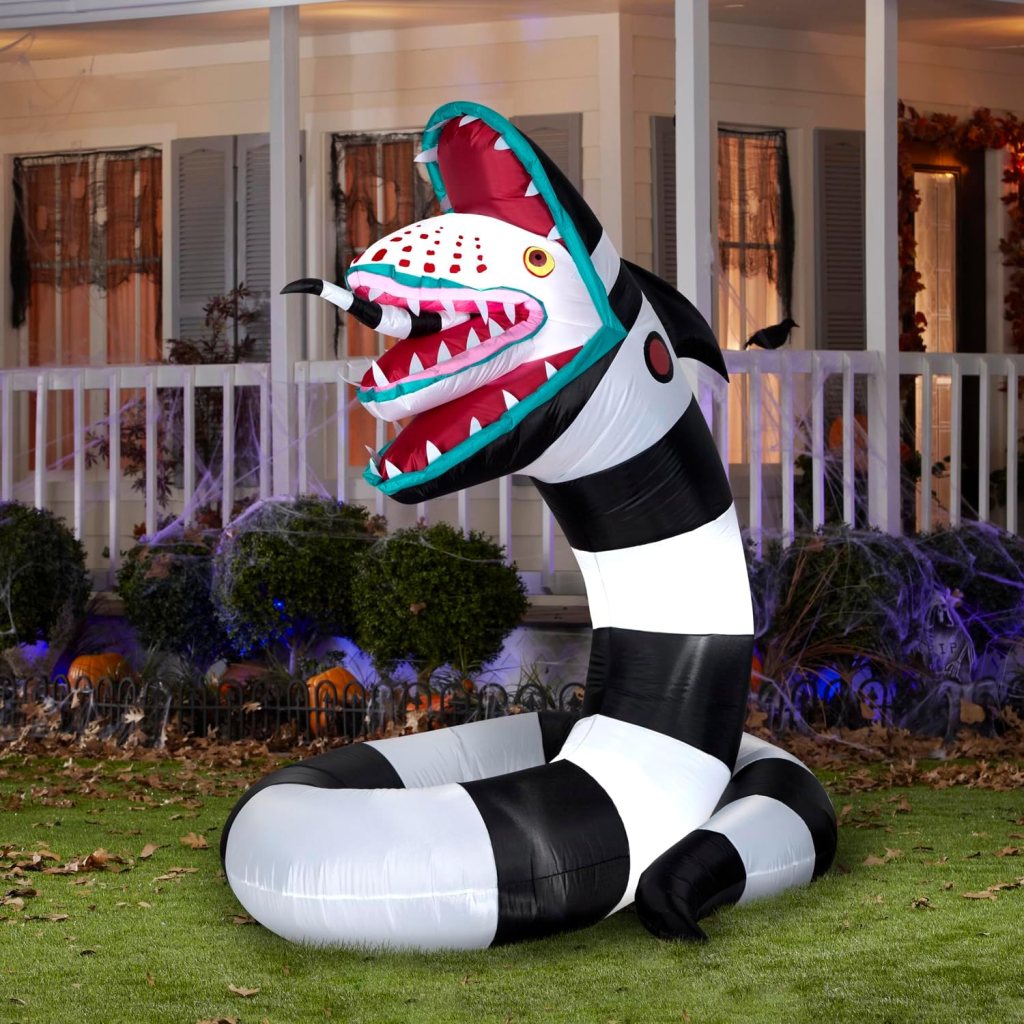 A large inflatable snake decoration with a striped black and white body and a colorful, menacing head, set up in a front yard during Halloween.
