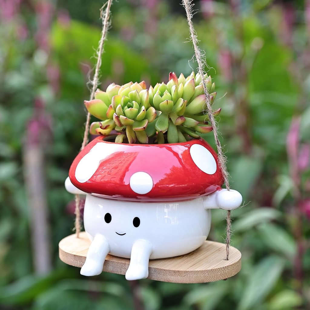 A whimsical hanging planter shaped like a mushroom with a red and white cap, featuring succulent plants inside and a smiling face.