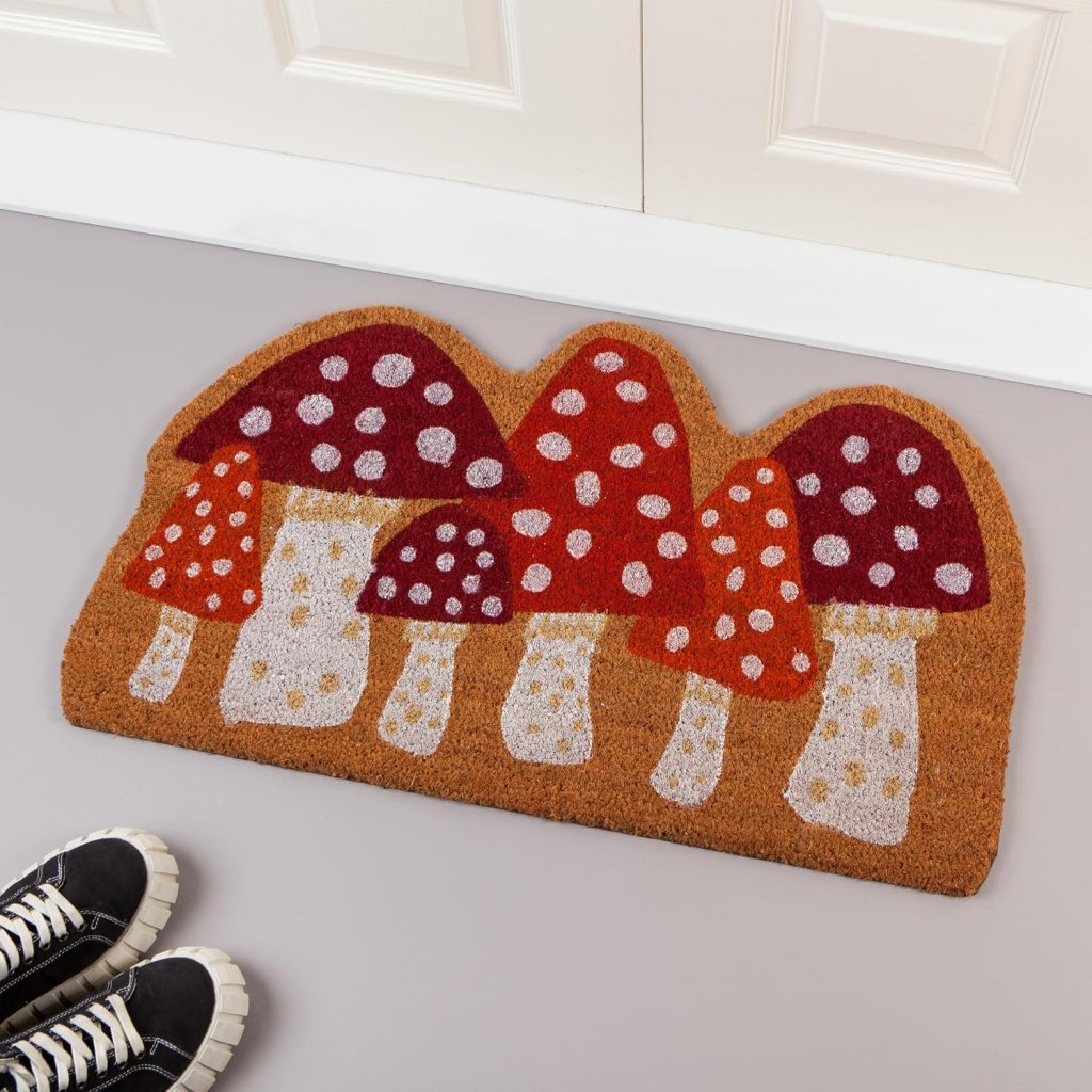 A colorful doormat featuring a design of various mushrooms with white polka dots on a brown background, placed in front of a doorway.