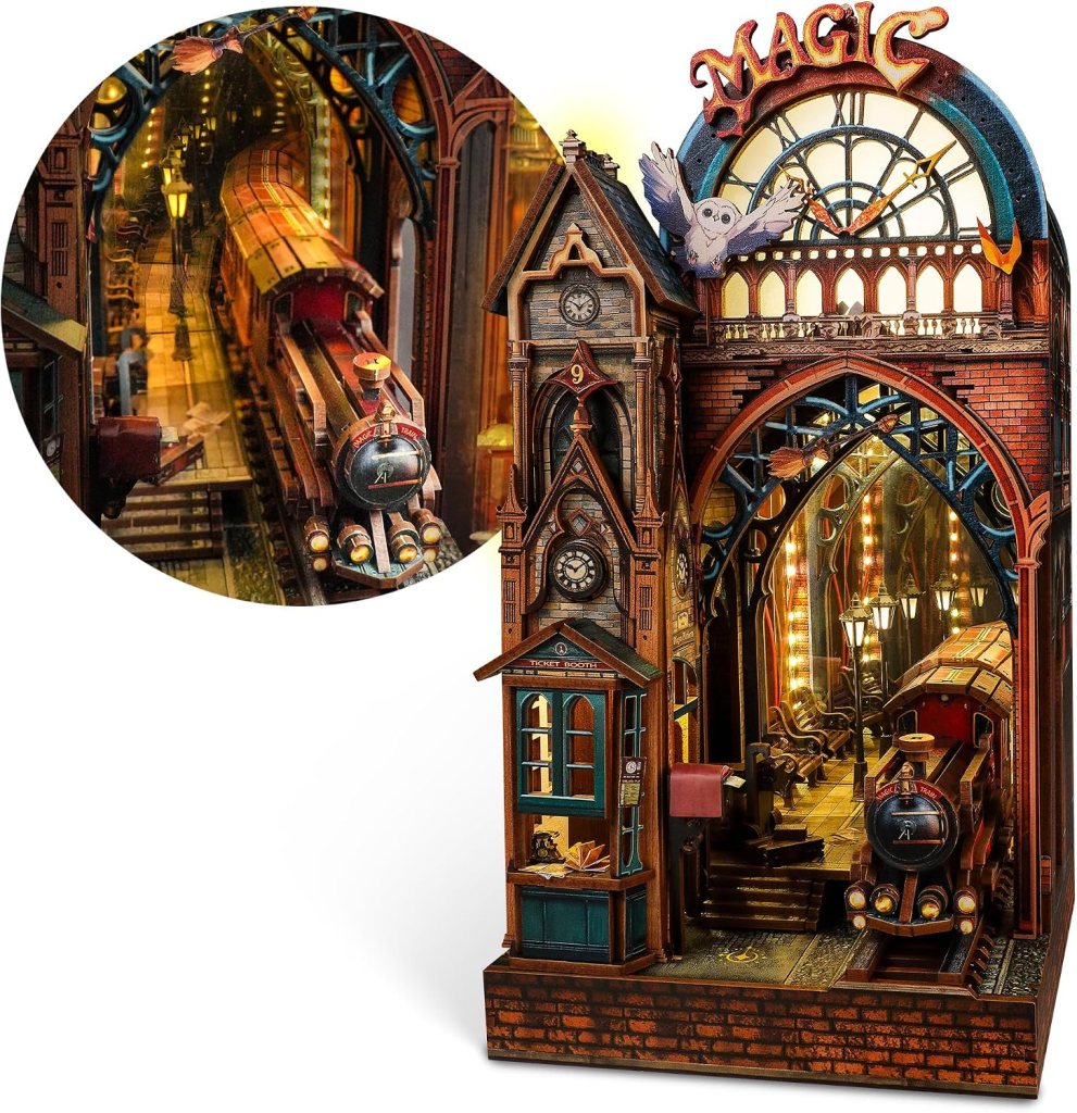 A detailed miniature of a magical train station featuring a steam locomotive, ornate architecture, and a ticket booth, with an owl perched above the entrance labeled 'Magic'.