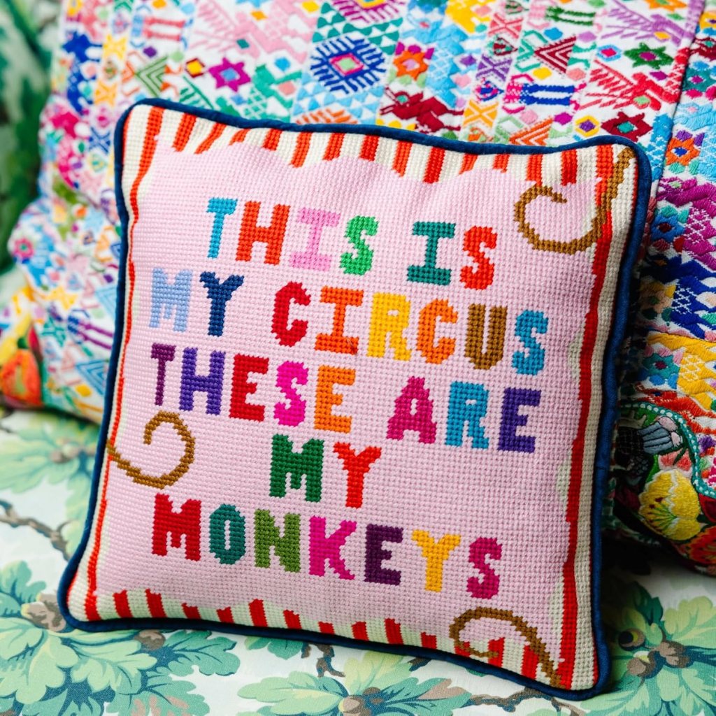 A decorative pillow featuring the text 'THIS IS MY CIRCUS THESE ARE MY MONKEYS' in vibrant, colorful letters against a pink background, with playful design elements.