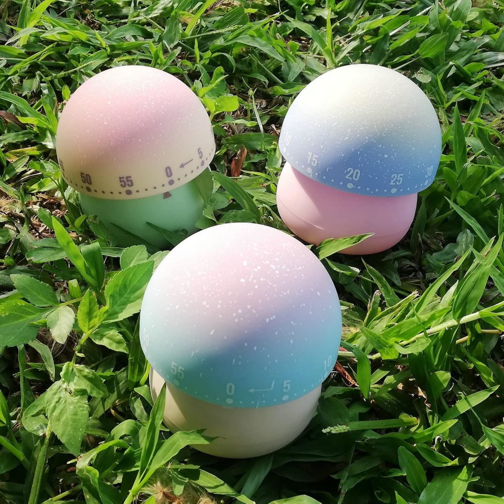 Three colorful, dome-shaped timers sitting on green grass, featuring pastel gradients and marked numbers.