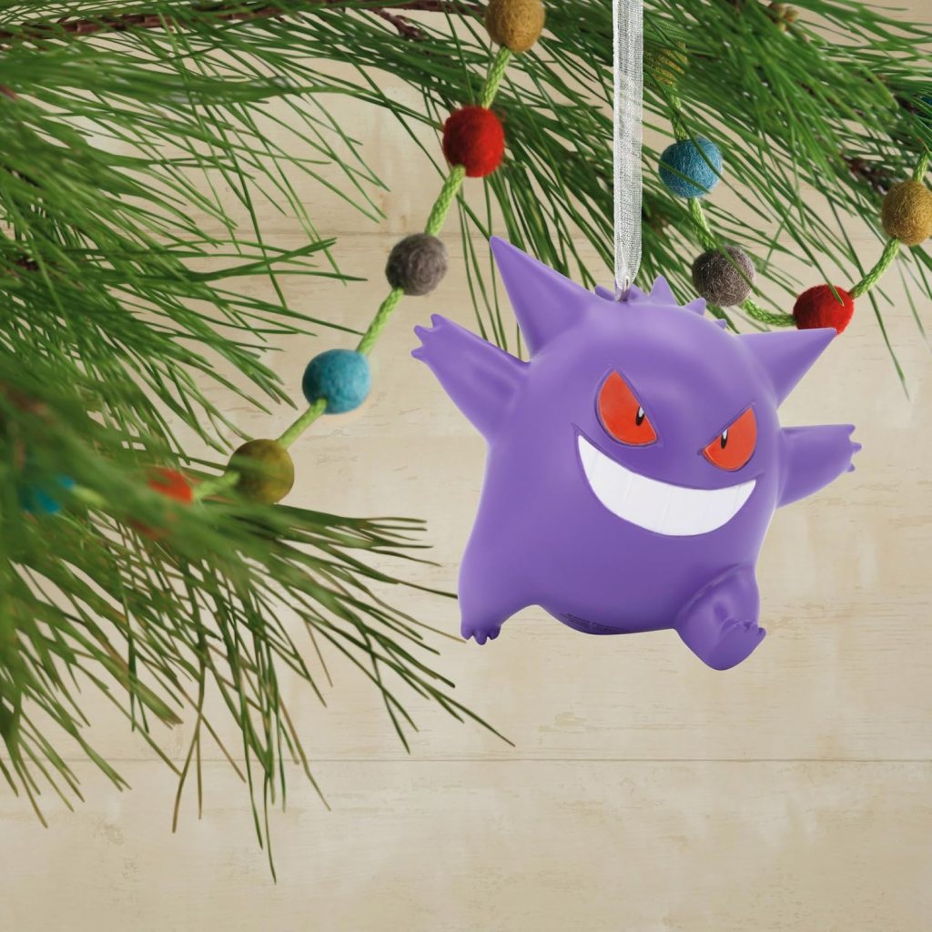 A purple ghost-like character with red eyes and a wide grin, hanging from a pine branch decorated with colorful pom-poms.