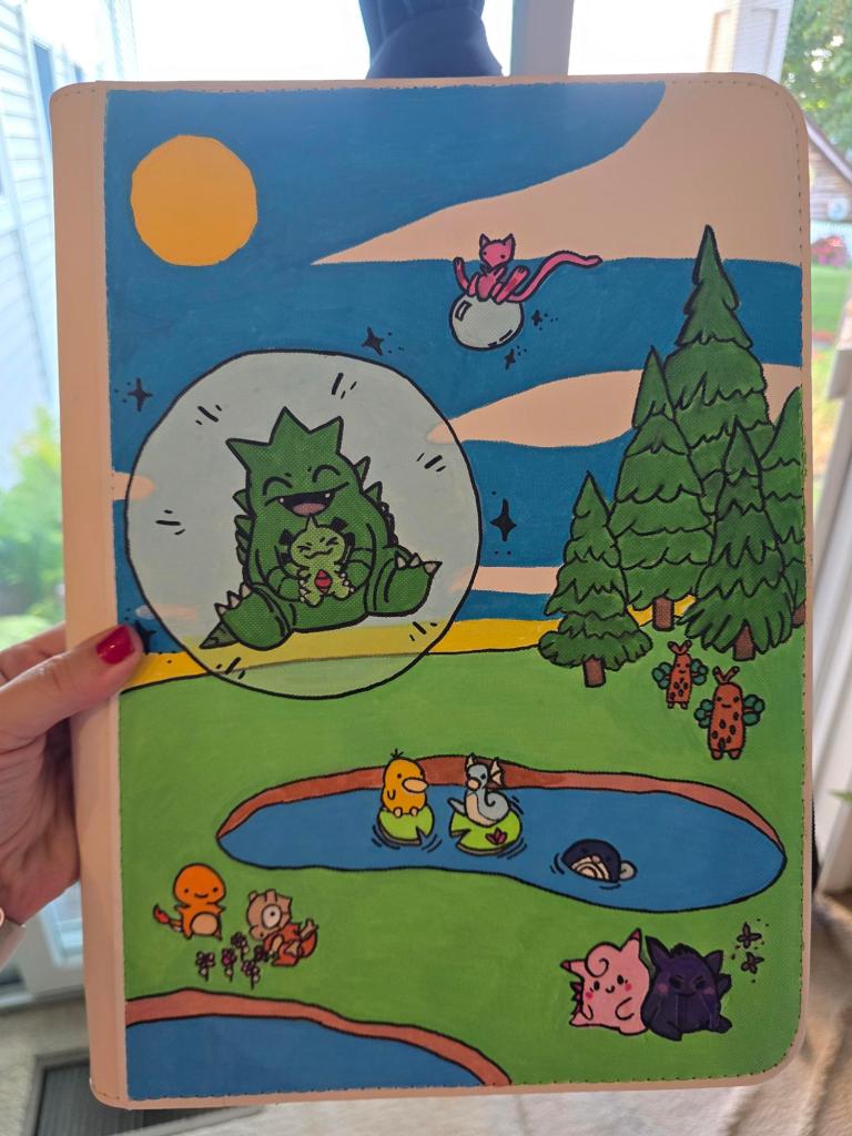 A colorful illustration on a notebook cover featuring various cute cartoon animals, including a green creature surrounded by a bubble, a pink cat on a moon, and several smaller animals by a pond in a whimsical landscape with trees and a bright sun.