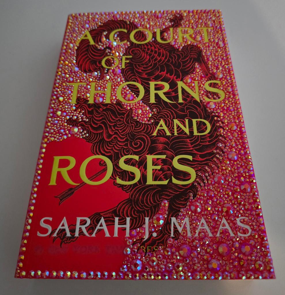 Close-up of the book cover for 'A Court of Thorns and Roses' by Sarah J. Maas, featuring a vivid red background adorned with intricate, sparkling designs.